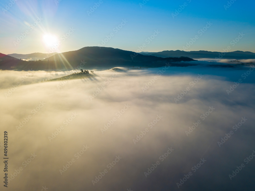 Obraz premium Flight over fog in Ukrainian Carpathians in summer. Mountains on the horizon. A thick layer of fog covers the mountains with a continuous carpet. Aerial drone view.
