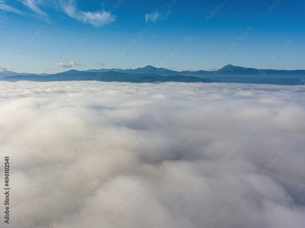 Flight over fog in Ukrainian Carpathians in summer. A thick layer of fog covers the mountains with a solid carpet. Mountains on the horizon. Aerial drone view.