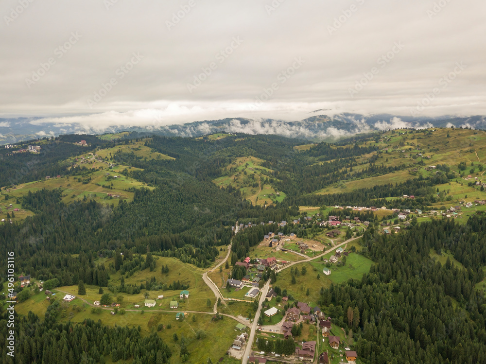Green slopes of Ukrainian Carpathian mountains in summer. Cloudy morning, low clouds. Aerial drone view.