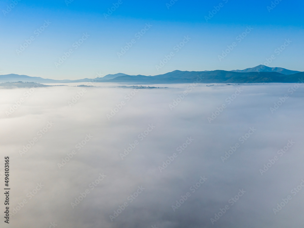 Flight over fog in Ukrainian Carpathians in summer. Mountains on the horizon. A thick layer of fog covers the mountains with a continuous carpet. Aerial drone view.