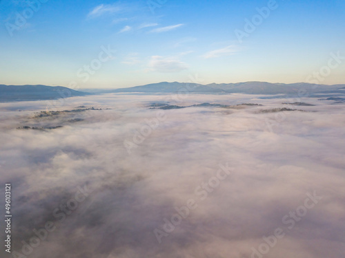 Flight over fog in Ukrainian Carpathians in summer. A thick layer of fog covers the mountains with a solid carpet. Mountains on the horizon. Aerial drone view.