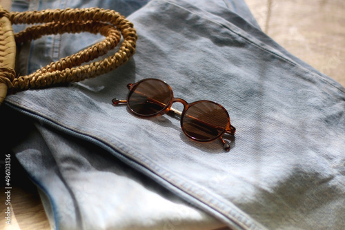 Vintage mom jeans, round straw bag and sunglasses on wooden background. Selective focus.