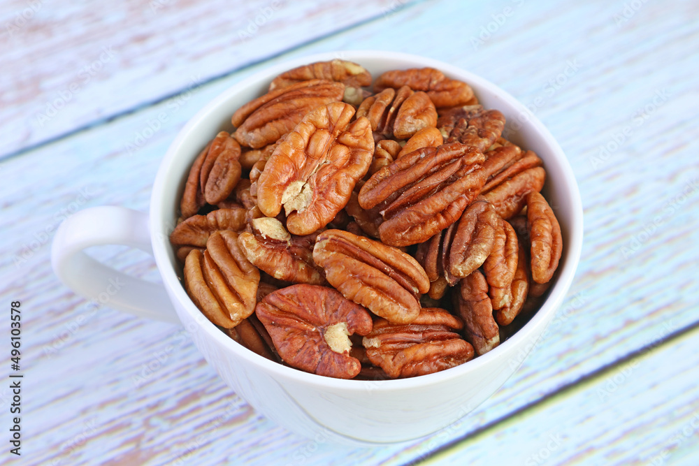 Close-up a Cup Filled with Pecan Nuts Isolated on Pale Blue Wooden Table Close-up a Cup Filled with Pecan Nuts Isolated on Pale Blue Wooden Table