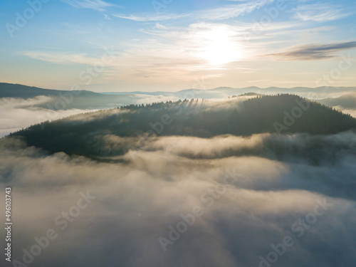Sunny morning in the foggy Carpathians. A thin layer of fog covers the mountains. Aerial drone view. © Sergey