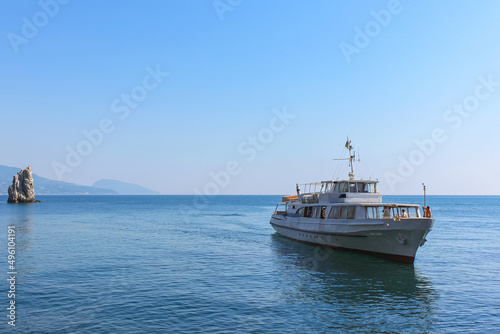 The pleasure craft in the calm blue sea water. The background is a blue sky and mountains. Beautiful seascape. Excursion tourism. Yalta, Crimea.