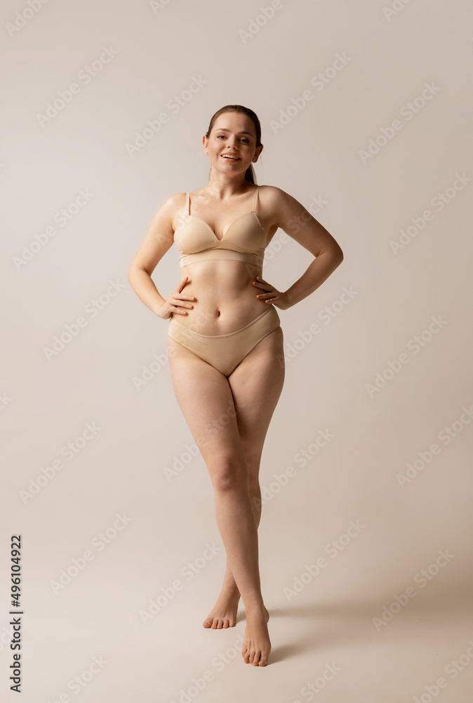 Fototapeta premium Full-length portrait of young beautiful woman posing in beige underwear isolated over studio background