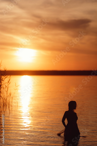 Silhouette of a beautiful girl at sunset in the river. A woman swims in the lake © V_Saratovtseva