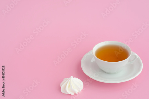 A cup of tea and marshmallows on a pink table background, copy space. Black tea and sweets, tea time