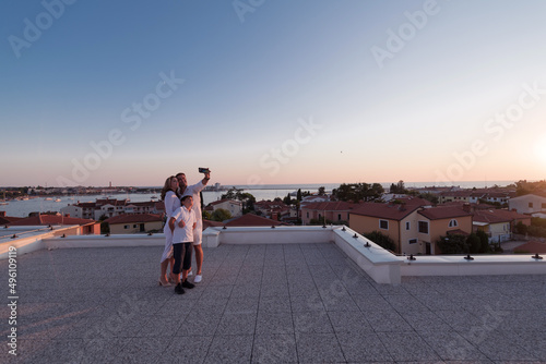 Happy family taking a selfie with a smartphone on the roof of their house at sunset. Selective focus 