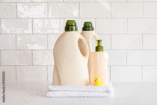 Set of laundry detergent bottles, clean towels and duck toy on table in bathroom.