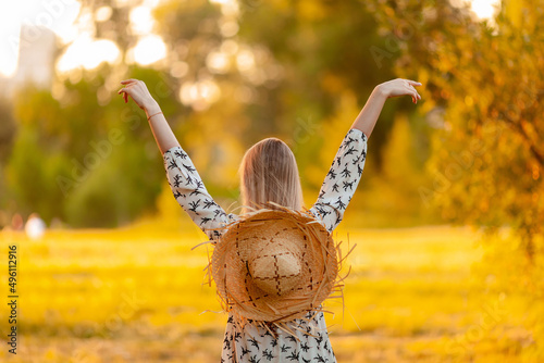 blonde with a straw hat rejoices in summer, view from the back