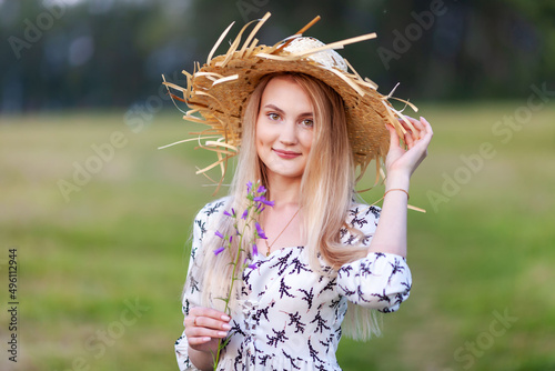 blonde young woman in a light summer dress with a straw hat