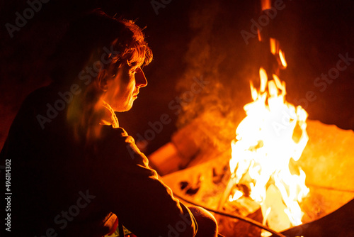 young man sitting near fire in camping in summer night