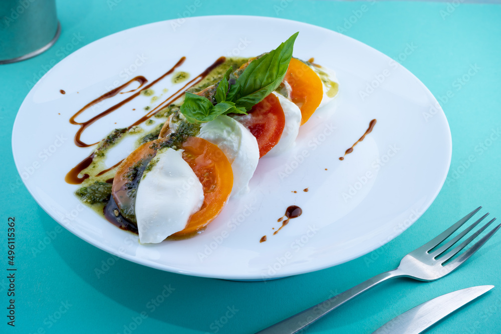 Caprese salad with tomatoes, mozzarella and basil. Red and orange tomatoes with white cheese and sauce. Portion of food on a plate in a restaurant. View from above. Delicious healthy food. Caprese salad with tomatoes, mozzarella and basil. Red and orange tomatoes with white cheese and sauce. Portion of food on a plate in a restaurant. View from above. Delicious healthy food.