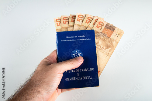 Hand holding Brazilian document work and social security (Carteira de Trabalho e Previdencia Social) with fifty reais banknotes. brazilian money