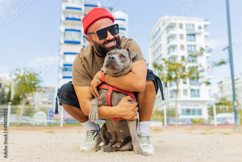 Cheerful multicultural race man in eyeglases playing with his dog in sity park photo