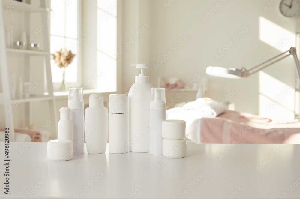 Cosmetic products of new professional female bodycare line for skin care, health, beauty and wellbeing. White mockup bottles, jars and soap dispenser with pump lid standing in row on table in spa room Cosmetic products of new professional female bodycare line for skin care, health, beauty and wellbeing. White mockup bottles, jars and soap dispenser with pump lid standing in row on table in spa room