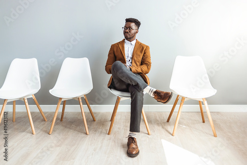 Male entrepreneur waiting for job interview in a hallway. He's the last one left to be interviewed. Full length studio shot of a handsome young businessman sitting against a gray background photo