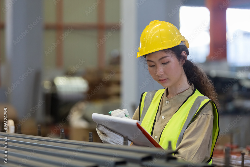 Fototapeta premium women engineer take notes on paperwork quality control standing at machine of factory warehouse.