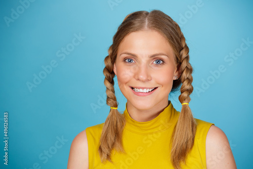 Close up portrait of young attractive smiling girl with pigtails standing isolated over blue background