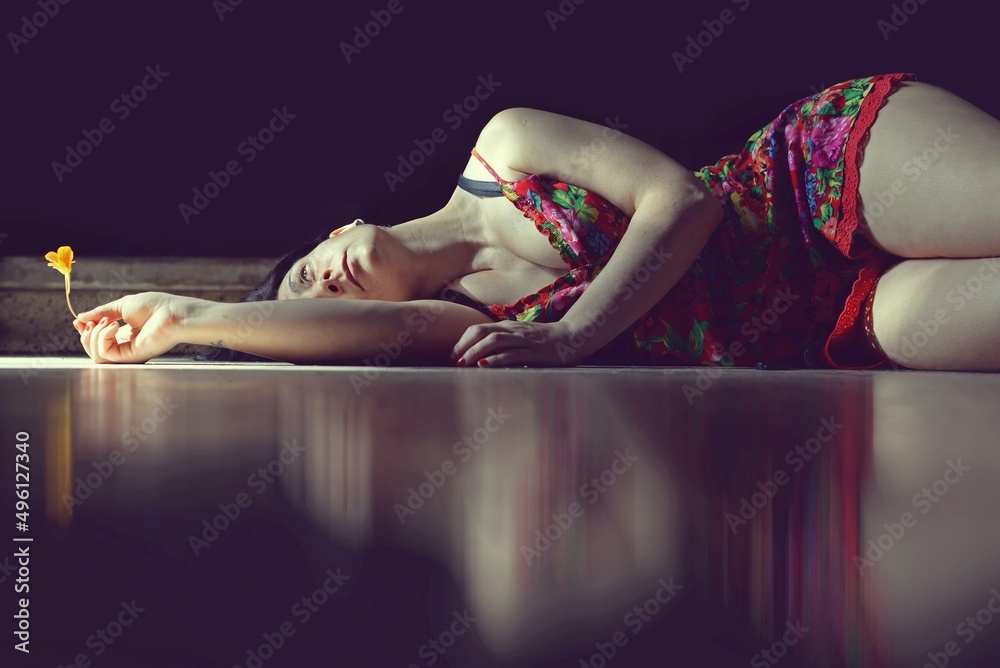 Autorretrato, mujer recostada en el suelo con una flor naranja en la mano.  foto de Stock | Adobe Stock