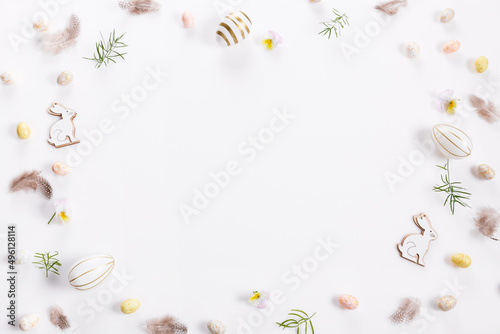 Festive Easter border, frame made of Easter eggs and feathers on a white background. Stylish easter flat lay in white color.
