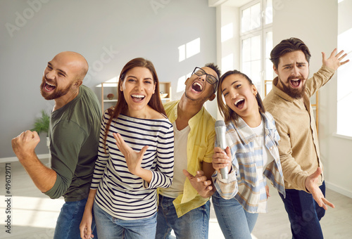 Friendship, home entertainment and people. Positive fun company of friends singing their favorite songs together on karaoke microphone during home party. Multiracial young people have fun together.