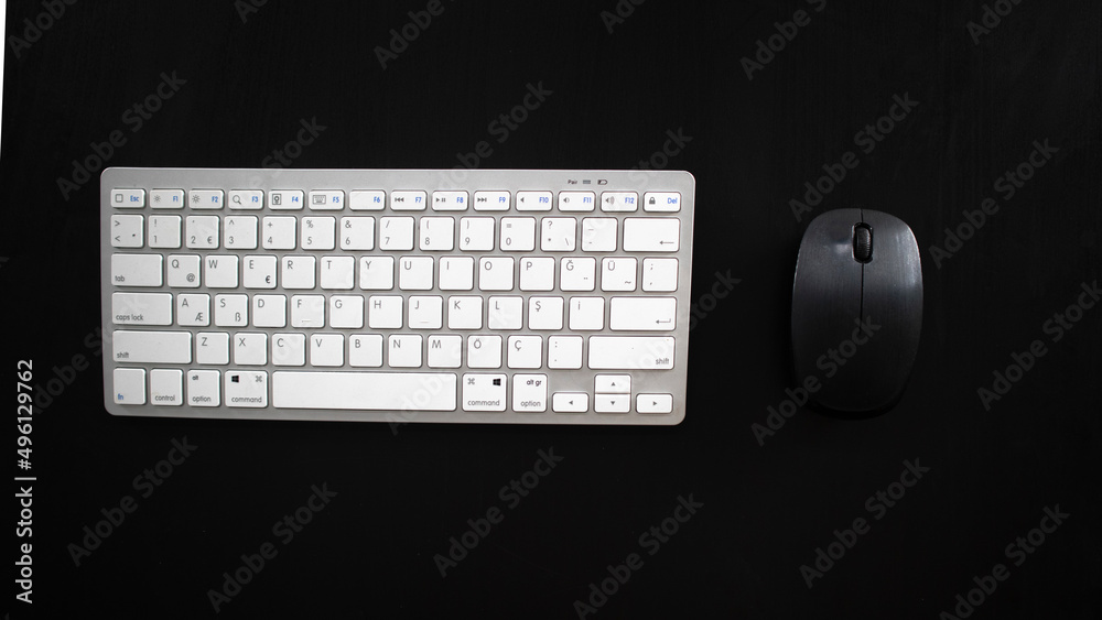 White wireless keyboard and black mouse on desk, isolated on black background, top view White wireless keyboard and black mouse on desk, isolated on black background, top view