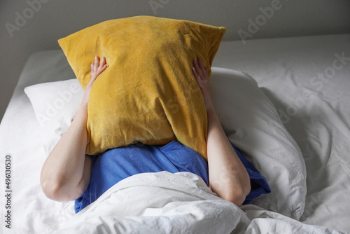 tired listless person lying in bed and hiding face under pillow