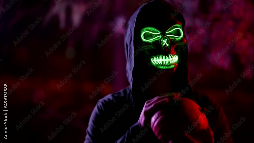 portrait of a person in a terrible glowing mask of death and in a cape with a hood against the background of branches illuminated by red light. the character pressed the skull and stroked it. dark key portrait of a person in a terrible glowing mask of death and in a cape with a hood against the background of branches illuminated by red light. the character pressed the skull and stroked it. dark key