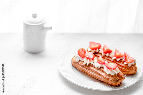 Eclairs with cream and strawberries on a white plate. 
