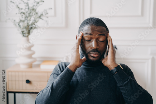 Stressed young african man employee with frustrated face expression suffering from headache
