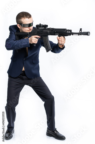 a guy in fashionable interactive glasses, in a business suit with a machine gun aims to the side. on a white background. civilians with weapons, took up arms, on the warpath photo