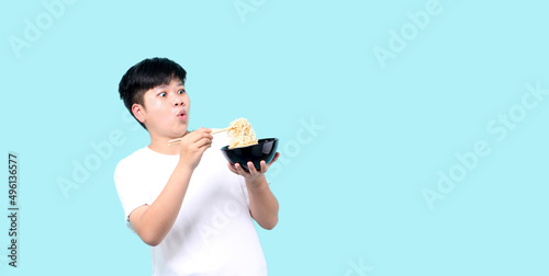Close up tomboy Asian eating yummy hot and spicy instant noodle using chopsticks and bowl isolated on blue background in studio With copy space.