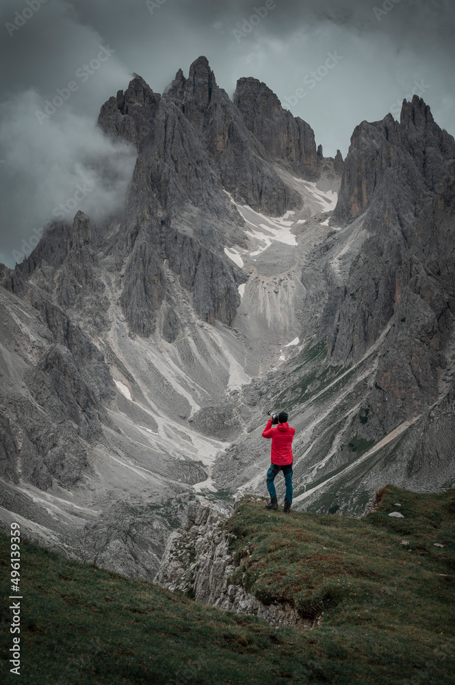 Photographer with camera and red jacket in front of Dolomite Alps at Three Peaks in Italy, low clouds passing by Dolomite mountains.