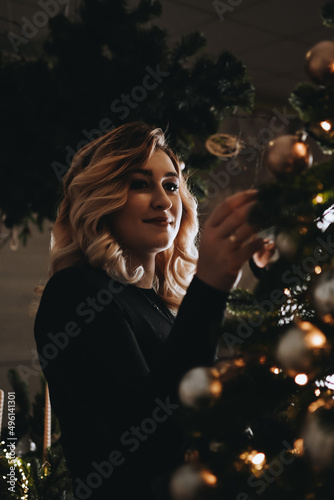 Portrait of a young blonde woman against the backdrop of the Christmas tree. Cozy home interior. Holiday celebration.