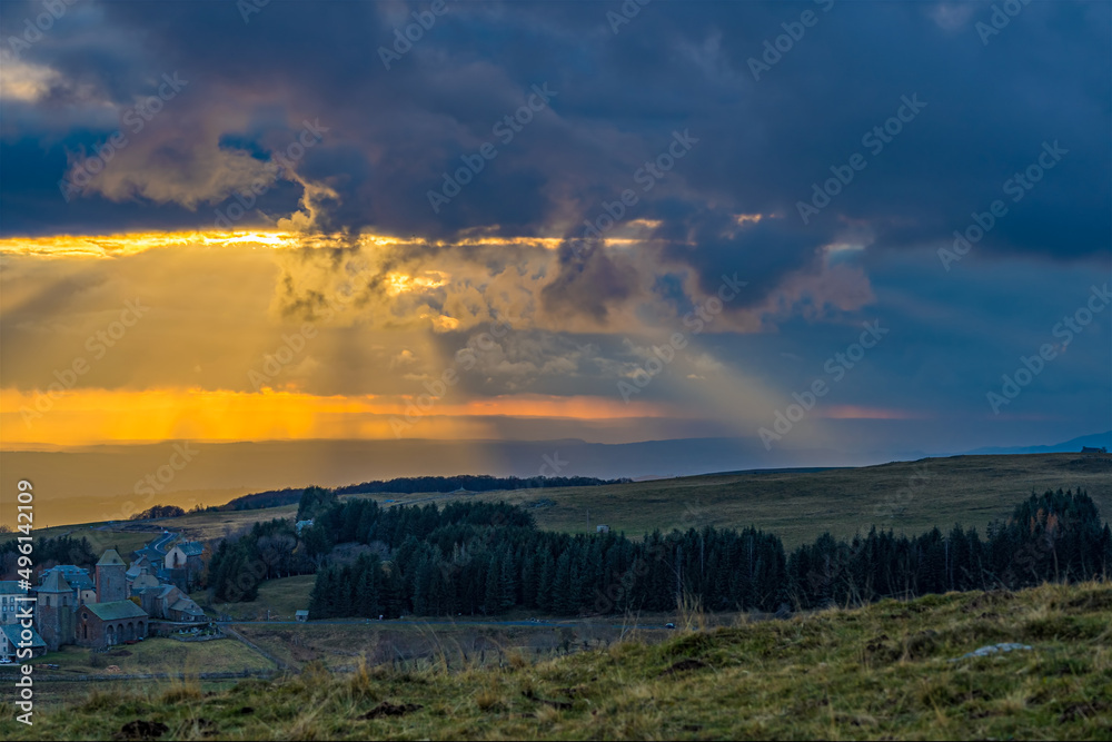 Sunshine Through Stormy Clouds With Yellow Sky Above French Mountain With Firs 