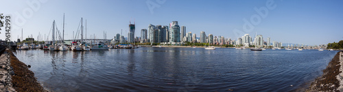Vancouver city skyline reflected in the water. Tall office buildings mirrored. Busy city life viewed from afar. Tranquil water. Blue skies. 