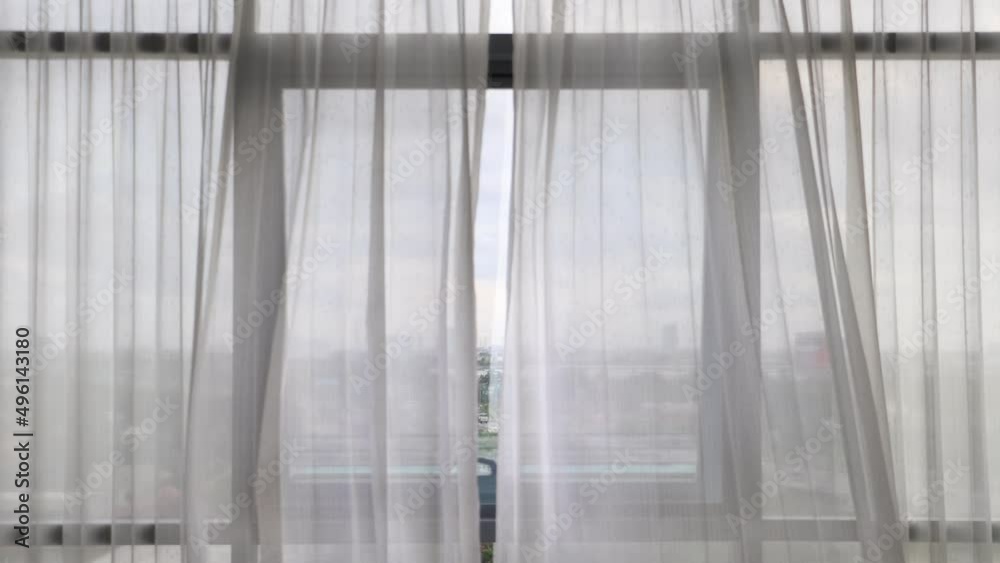 Curtains flutter in the wind from an open window in a wall of square windows