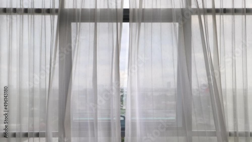 Curtains flutter in the wind from an open window in a wall of square windows