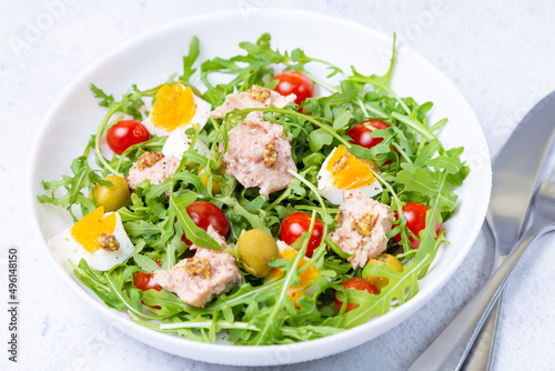 Salad with tuna, arugula, tomatoes, olives and eggs in a white plate. A traditional dish. Close-up.