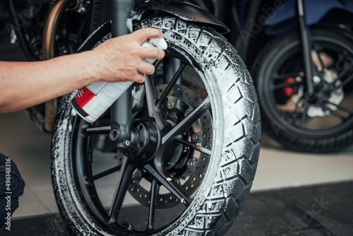 Man washing motorcycle or scooter and spraying snow foam on Tyre wheels .Tyre restoration maintenance ,repair motorcycle concept in garage .selective focus