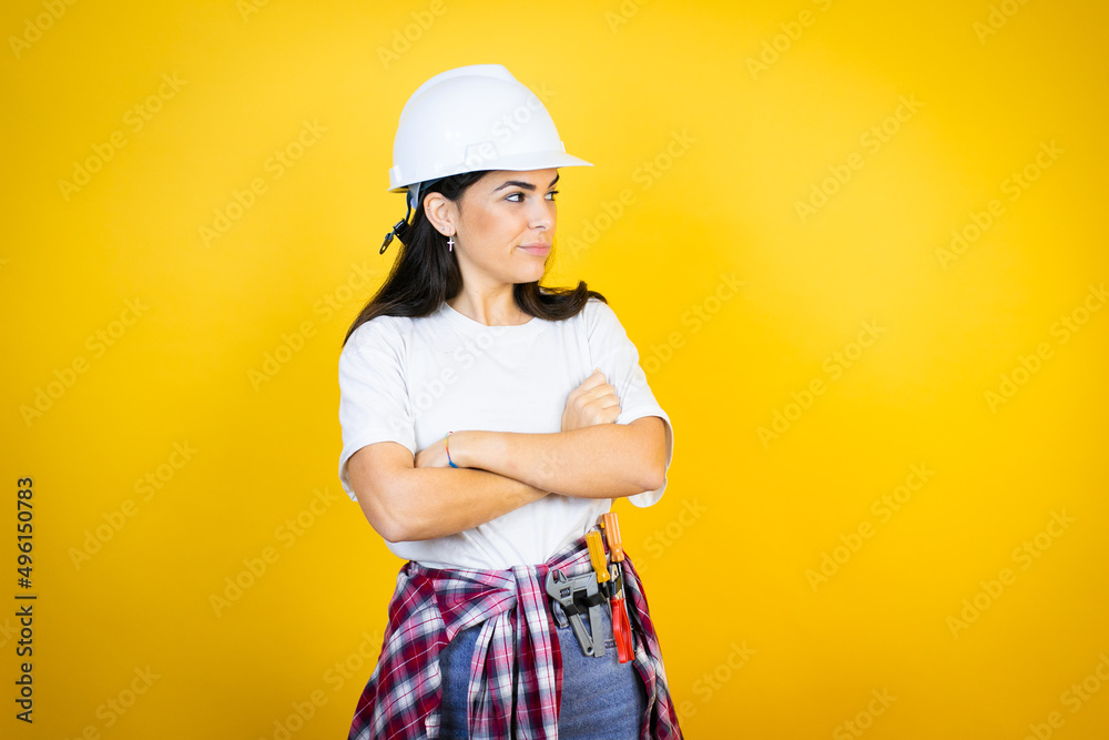 Young caucasian woman wearing hardhat and builder clothes over isolated yellow background thinking looking tired and bored with crossed arms Young caucasian woman wearing hardhat and builder clothes over isolated yellow background thinking looking tired and bored with crossed arms