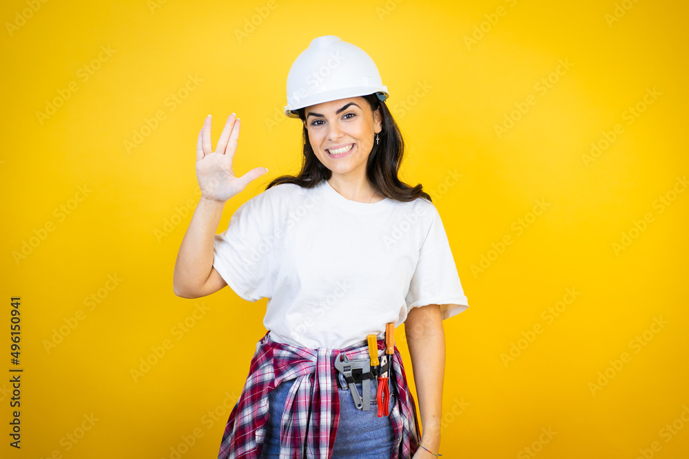 Young caucasian woman wearing hardhat and builder clothes over isolated yellow background doing star trek freak symbol Young caucasian woman wearing hardhat and builder clothes over isolated yellow background doing star trek freak symbol