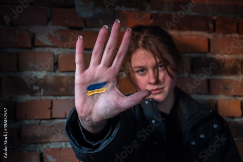 A girl stands on the wall background of her ruined house with a painted flag of ukraine on her palm. Stop War. Peace in Ukraine.  No war, stay with Ukraine. Selective focus
