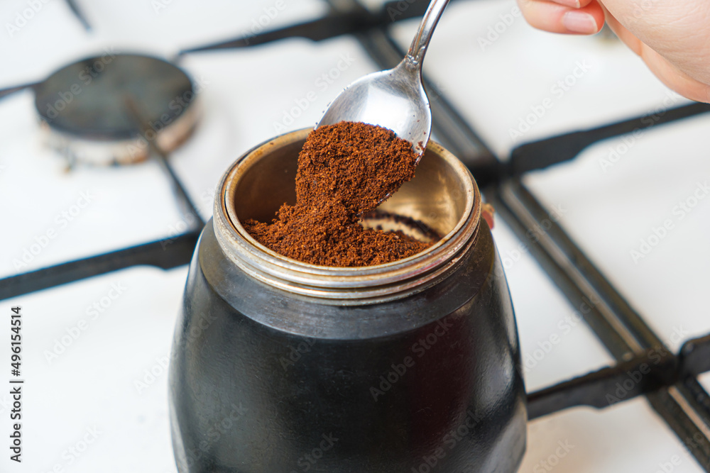 The process of pouring ground fresh coffee into a geyser coffee maker standing on a gas stove The process of pouring ground fresh coffee into a geyser coffee maker standing on a gas stove