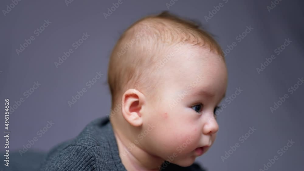 Lovely Caucasian boy with adorable cheeks looking curiously around. Beautiful baby portrait close up. Grey blurred backdrop. Lovely Caucasian boy with adorable cheeks looking curiously around. Beautiful baby portrait close up. Grey blurred backdrop.