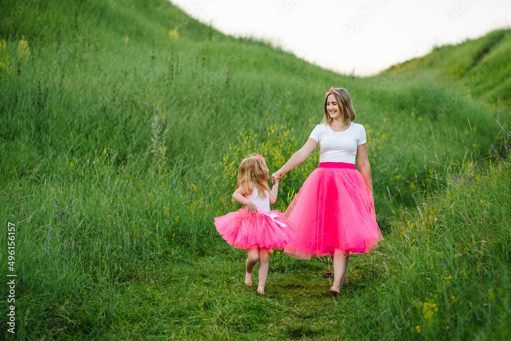 Mom with daughter in pink dresses and barefoot walking in the field. A young beautiful mother with a daughter in the same clothes. Family same look. Fashion style. Clothing for parent and child.