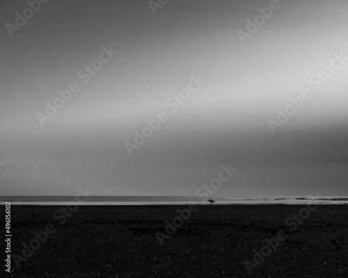 A lone surfer walks along the shoreline of Belhaven Bay looking at the North Sea for good waves
