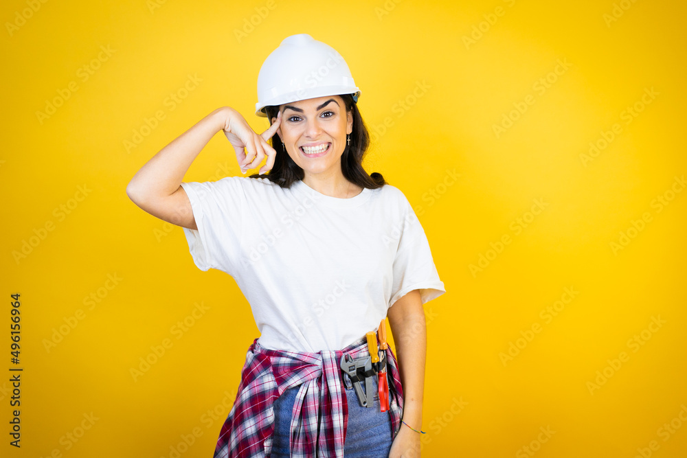 Young caucasian woman wearing hardhat and builder clothes over isolated yellow background smiling and thinking with her fingers on her head that she has an idea.